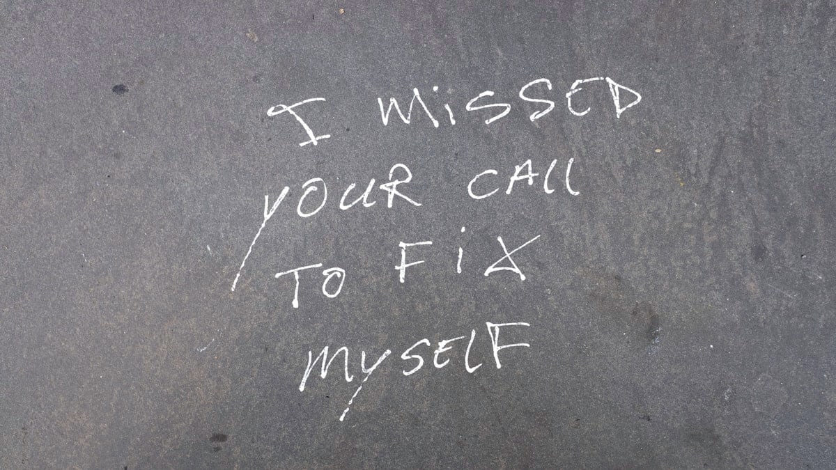 Written directly on dark pavement in rough white chalk, the message “I MISSED YOUR CALL / TO FIX / MYSELF” reads like a personal confession left out in the open, turning the sidewalk into a temporary diary page.